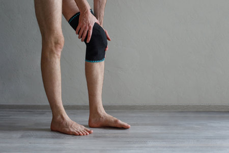 Male leg dressed in knee brace to help promote recovery of bones, muscles, ligaments. Man is feeling pain in joints after injury. Arthritis and meniscus diseases concept.の写真素材