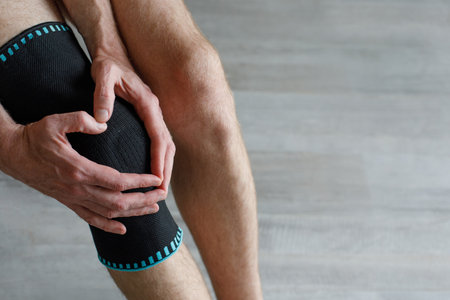 Black knee support brace on a man leg. Guy in an orthosis at home. Orthopedic anatomic braces for...