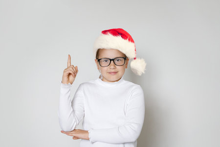 Christmas kid girl in red Santa hat pointing up on white backgroundの写真素材