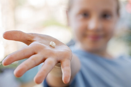Fallen baby tooth in hand of happy little girl. The concept of hygiene of baby teeth