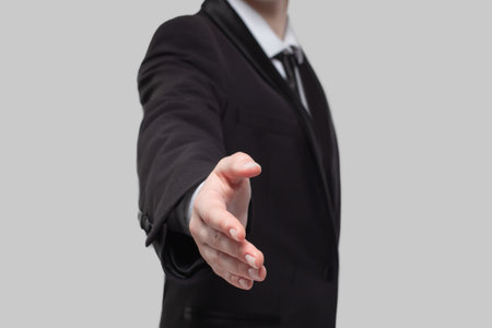 Business person in suit shaking hand on gray studio wall backgroundの写真素材