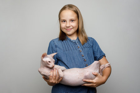 Cute little child in blue dress holding cat against gray studio wall banner backgroundの写真素材