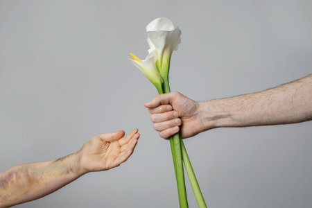 Male hand with flower and female hand with bruise. Campaign stop violence against womenの写真素材