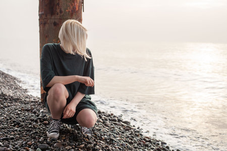 Casual young woman with blonde hair sitting on sea beachの写真素材