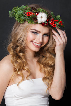 Laughing blonde woman portrait. Fashion female model with blond curly hairstyle, make-up and green and red winter accessories posing on black backgroundの写真素材