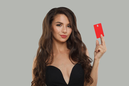 Cheerful model brunette lady holding debit card looking at camera isolated on gray studio wall banner backgroundの写真素材