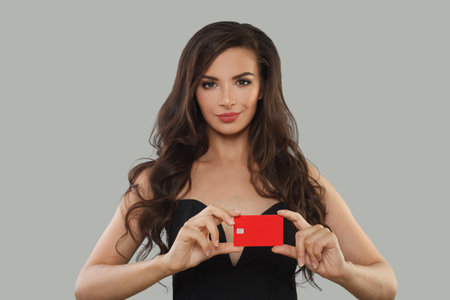 Beautiful brunette woman holding in her hand bank card solution isolated over gray color studio wall backgroundの写真素材