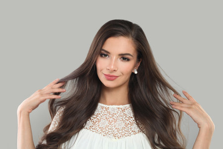 Cute fashion model with dark healthy hairstyle, fresh clean skin and trendy make-up looking at camera on gray background. Brunette woman portraitの写真素材