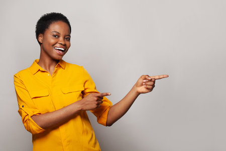 Cheerful woman pointing finger at light gray studio wall banner backgroundの写真素材