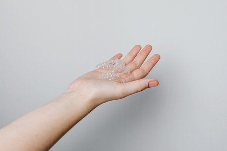 Hand with Invisible aligners for whitening and straightening of teeth on white background....