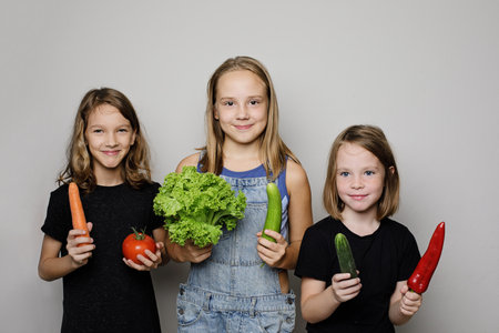 Happy children with vegetables on white studio wall banner background. Child girls with fresh organic food portrait, healthy eating conceptの写真素材