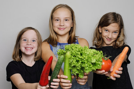 Portrait of beautiful children holding vegetables on white studio wall banner background. Child girls with fresh organic food portrait, healthy eating conceptの写真素材
