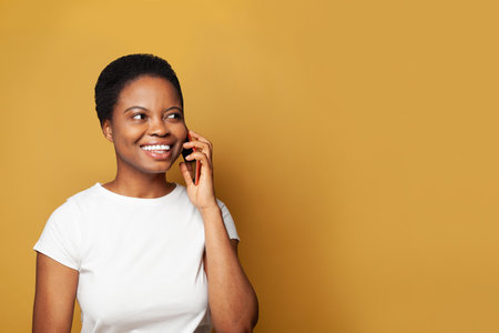 Young woman talking by phone on bright yellow banner backgroundの写真素材