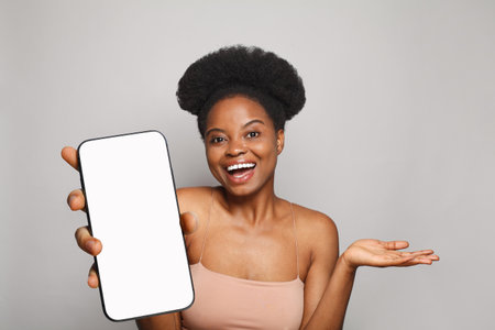 Perfect healthy woman holding smartphone with white empty blank screen display on gray studio wall background. Happy model with phoneの写真素材