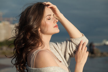 Pretty young lady brunette model on sea beach. Beauty woman with makeup and long dark wavy hairstyle outdoors. Tranquility emotion mood, travel, season and holiday conceptの写真素材