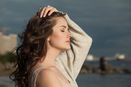 Summer brunette woman with fresh skin, natural make-up and healthy wavy brown hair enjoying the sunny morning and sea air. Female model outdoor fashion portraitの写真素材
