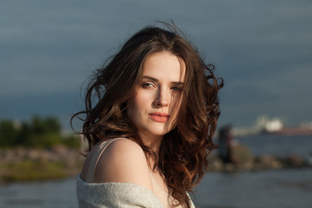 Attractive young woman model with brown hair and natural make-up walking along the shore of the resort on a spring morning. Happiness, balance, tranquility, emotion and mood conceptの写真素材