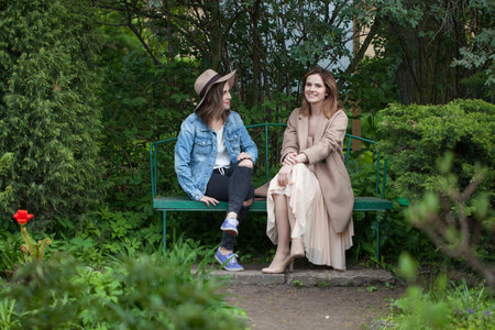 Best friends talking and sitting on a park bench outdoorsの写真素材