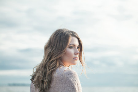 Perfect young adult woman with natural make-up and long wavy brown hair on blue sea beach outdoor...