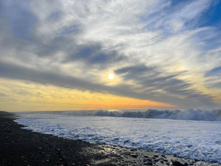 Sunset on the seashore. Empty beach, black sand, sea wave, sun and sky cloud backgroundの写真素材