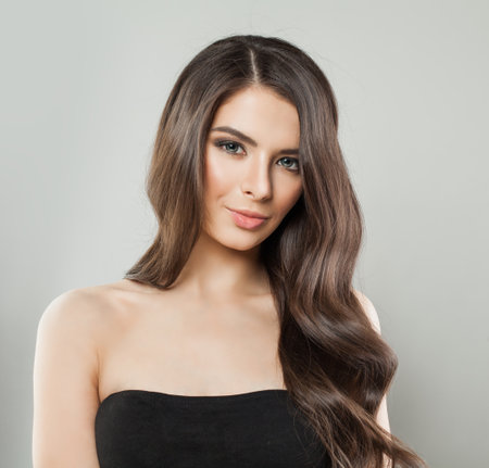 Cheerful young adult model woman with long healthy hairstyle, fresh shiny clear skin and makeup posing on white background. Beautiful female face close upの写真素材