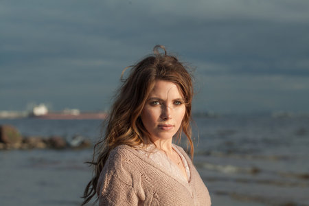 Healthy young adult woman with natural make-up and long wavy brown hair on blue sea beach outdoor portraitの写真素材