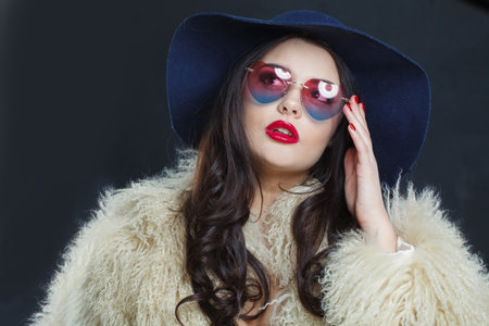 Perfect fashion model woman with long dark wavy hairstyle and red lips make-up wearing fashionable hat beauty studio portraitの写真素材