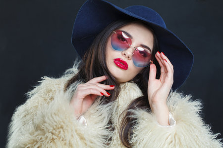 Elegant fashion model woman with long dark wavy hairstyle and red lips make-up wearing fashionable hat beauty studio portraitの写真素材