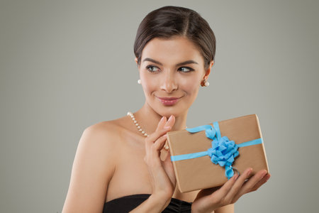 Nice young adult woman holding paper gift box on gray backgroundの写真素材