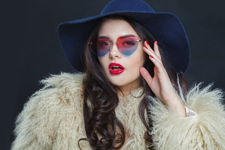 Successful fashion model woman with long dark wavy hairstyle and red lips make-up wearing fashionable hat beauty studio portraitの写真素材