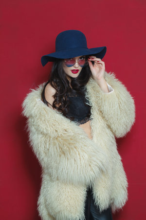 Standing fashion model woman with long dark wavy hairstyle and red lips make-up wearing fashionable hat beauty studio portraitの写真素材