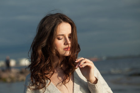 Gorgeous young lady brunette model on sea beach. Beauty woman with makeup and long dark wavy hairstyle outdoors. Tranquility emotion mood, travel, season and holiday conceptの写真素材