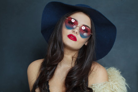 Excited fashion model woman with long dark wavy hairstyle and red lips make-up wearing fashionable hat beauty studio portraitの写真素材