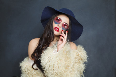 Posing fashion model woman with long dark wavy hairstyle and red lips make-up wearing fashionable hat beauty studio portraitの写真素材