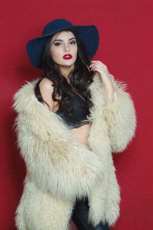 Sexy fashion model woman with long dark wavy hairstyle and red lips make-up wearing fashionable hat beauty studio portraitの写真素材