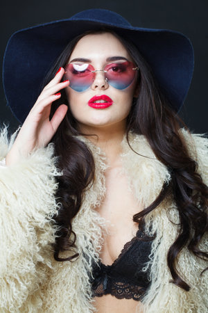 Fashion portrait of young adult woman fashion model with bright make-up and long wavy hair wearing blue hat and sunglasses posing against blue studio wall backgroundの写真素材