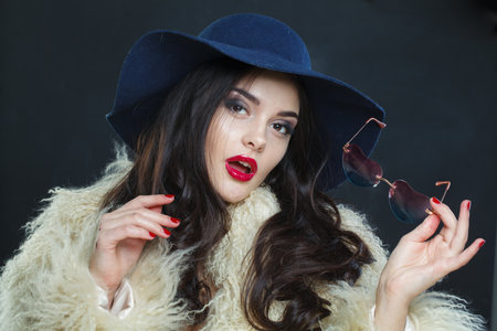 Charming fashion model woman with long dark wavy hairstyle and red lips make-up wearing fashionable hat beauty studio portraitの写真素材