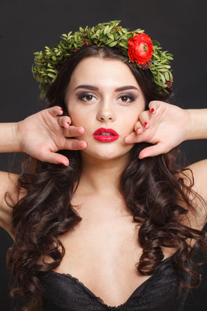 Gorgeous young woman with floral head wreath looking at camera while standing against black backgroundの写真素材