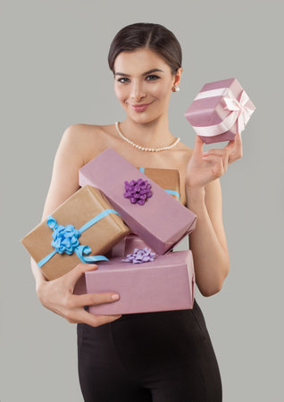 Attractive woman holding stack of gift present boxes standing against gray studio wall background. Shopping or holiday conceptの写真素材