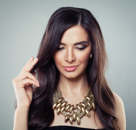Pretty woman with shiny silky brown hairstyle and gold jewelry necklace. Fashion studio portraitの写真素材