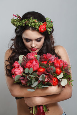 Spring portrait. Young beautiful woman in red flowers wreath posing agaist white backgroundの写真素材