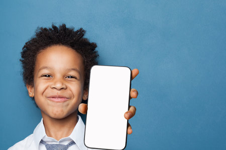 Cute child boy showing smartphone with empty display smiling on blue backgroundの写真素材