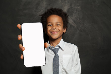 Smiling little school boy holding cell phone in his hand presenting smartphone empty screen display...
