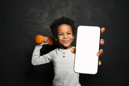 Active little school boy holding cell phone in his hand presenting smartphone empty screen display on blue studio wall background. Smartphone display mockupの写真素材