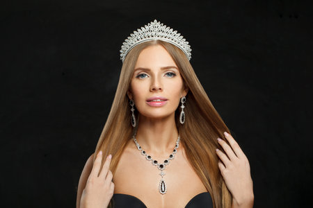 Beautiful jewelery model woman wearing stylish gold earring and necklace with blue crystal sapphire and diamond on black studio wall backgroundの写真素材