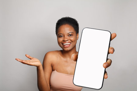 Surprised healthy woman holding smartphone with white empty blank screen display on gray studio wall background. Happy model with phoneの写真素材