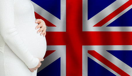 Demographics and pregnancy in UK concept. Close-up of pregnant woman belly against Flag of the United Kingdom background.の写真素材