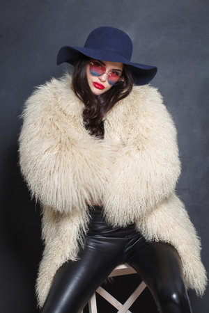 Glorious fashion model woman in blue classic hat and white fur coat posing indoor, elegance fashion beauty portraitの写真素材