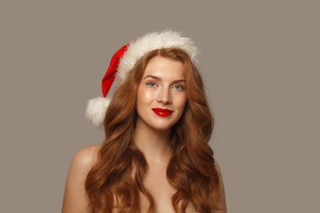 Beautiful Christmas woman in Santa hat with make-up and cute positive smile looking at camera, fashion portraitの写真素材