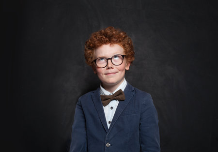 Intelligent child school boy in school uniform looking up on blackboard backgroundの写真素材